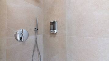 Un baño con ducha, un cabezal de ducha manual y un panel de control en la pared.