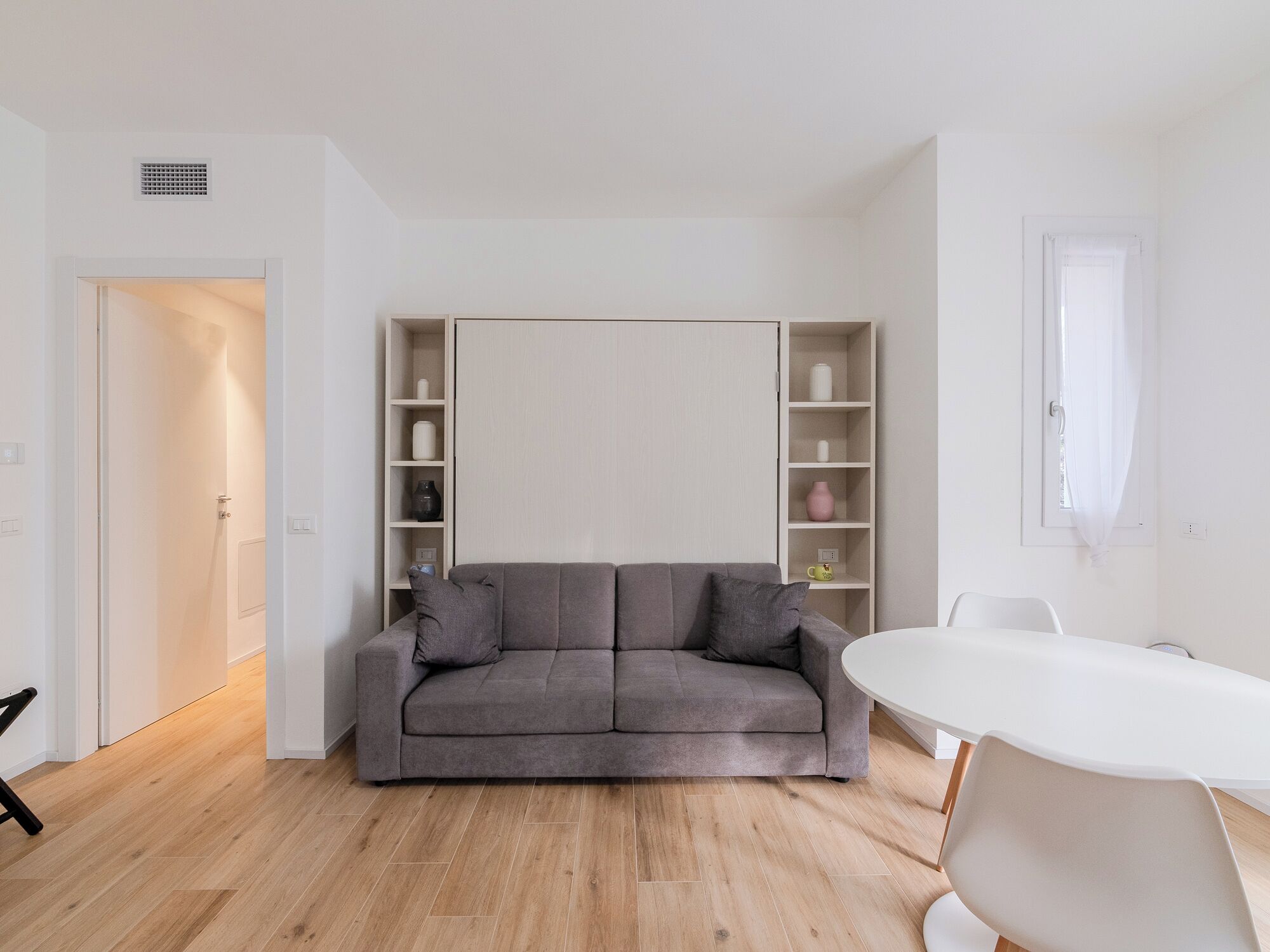 A modern living room with a grey sofa, white coffee table, and built-in shelving.