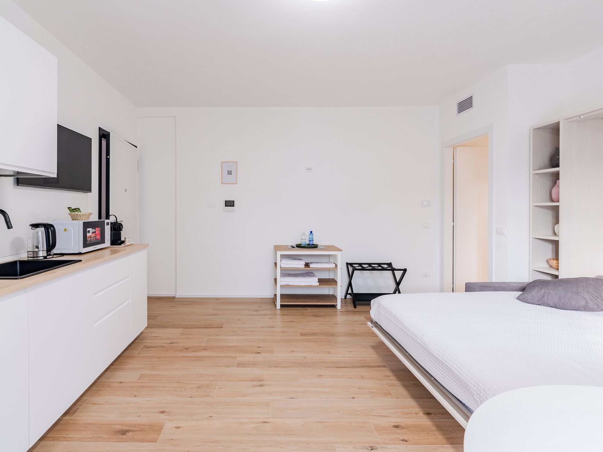 A modern, minimalistic bedroom with a bed, a small desk, and a kitchenette.