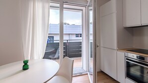 Una cocina moderna con armarios blancos, horno empotrado y puerta corredera de cristal que da a un balcón.