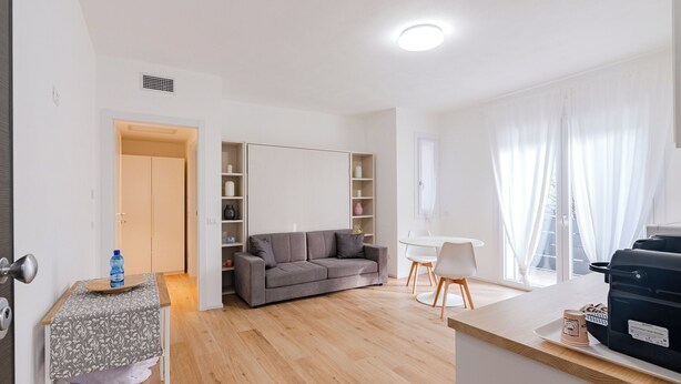 Una sala de estar moderna con un sofá, una mesa de comedor con sillas y una zona de cocina con mostrador y electrodomésticos.