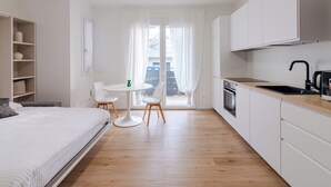 Una habitación de hotel moderna y minimalista, con una cama, una pequeña mesa redonda y una kitchenette.
