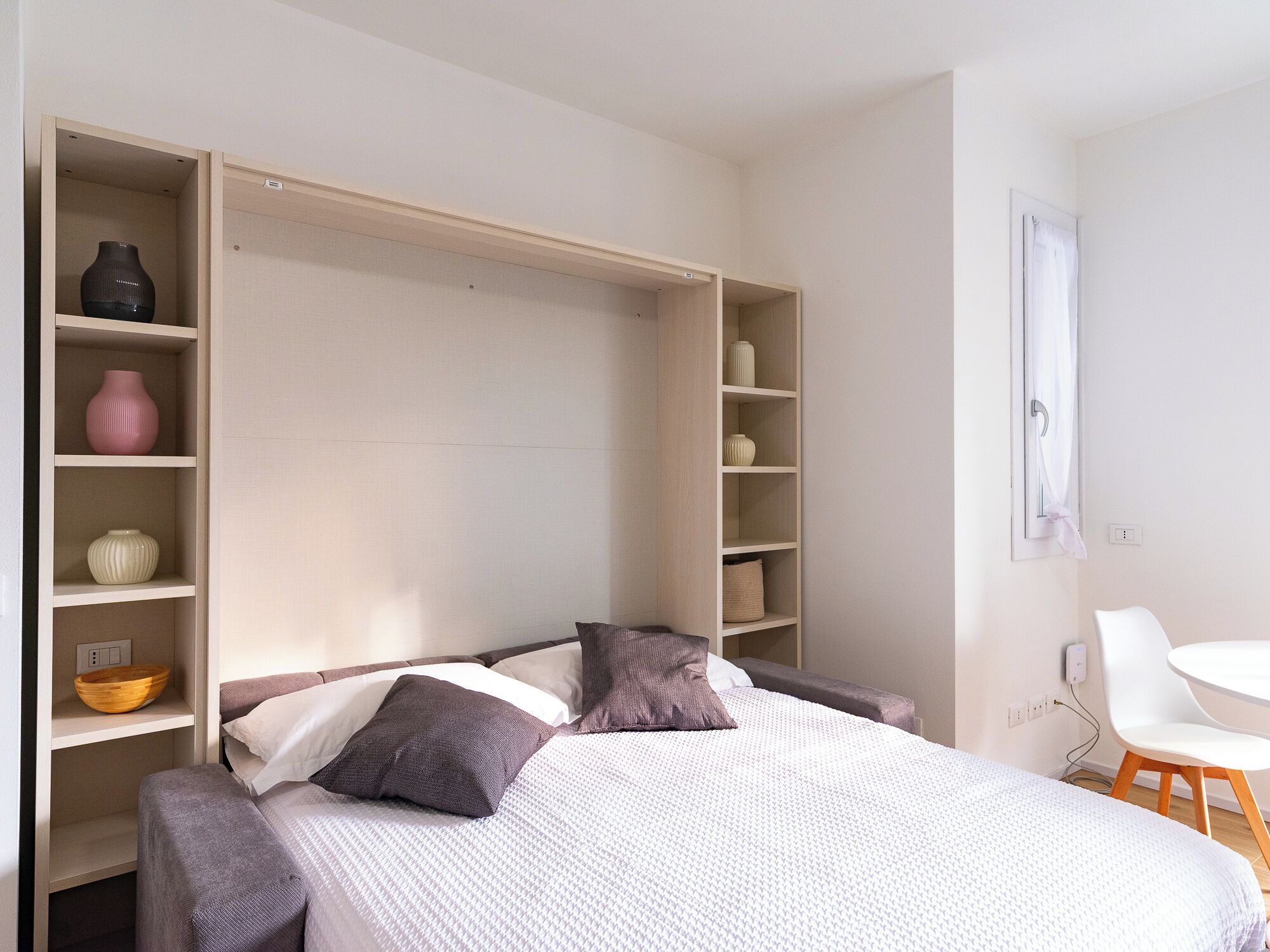 A bedroom with a bed, a built-in wardrobe, and a small table with a chair.