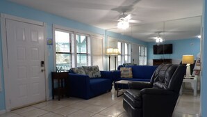 Ein Wohnzimmer mit einem blauen Sofa, einem schwarzen Ledersessel, einem kleinen Tisch und einem Deckenventilator.
