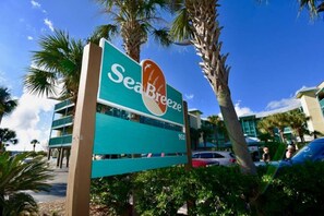 Schild für SeaBreeze mit Blick auf den Strand, Palmen und einem modernen Gebäude im Hintergrund.