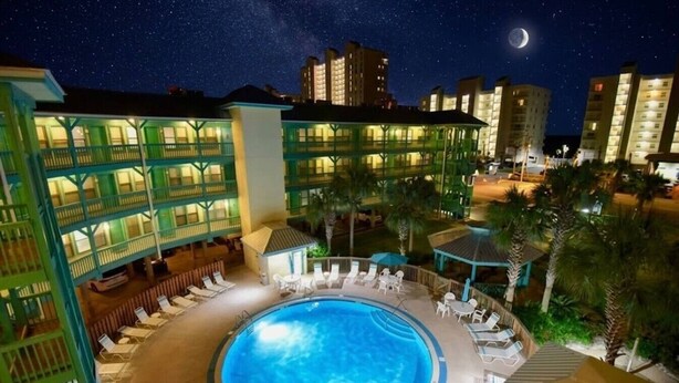 Ein Hotel mit Pool, mehreren Balkonen und einem sternenübersäten Nachthimmel mit Mond.