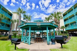 A gazebo with a sign, surrounded by palm trees and a building with balconies. - Gulf Shores - Sea Breeze 216 2/2 *Beach Access* (Gulf Shores)