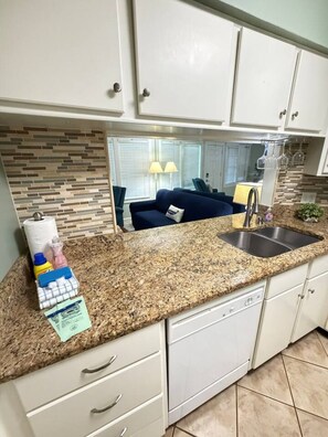 A kitchen with white cabinets, a granite countertop, a stainless steel sink, and a tiled backsplash. - Gulf Shores - Sea Breeze 216 2/2 *Beach Access* (Gulf Shores)