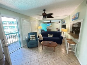 A living room with a sofa, armchair, coffee table, ceiling fan, and a view of the outside. - Gulf Shores - Sea Breeze 216 2/2 *Beach Access* (Gulf Shores)