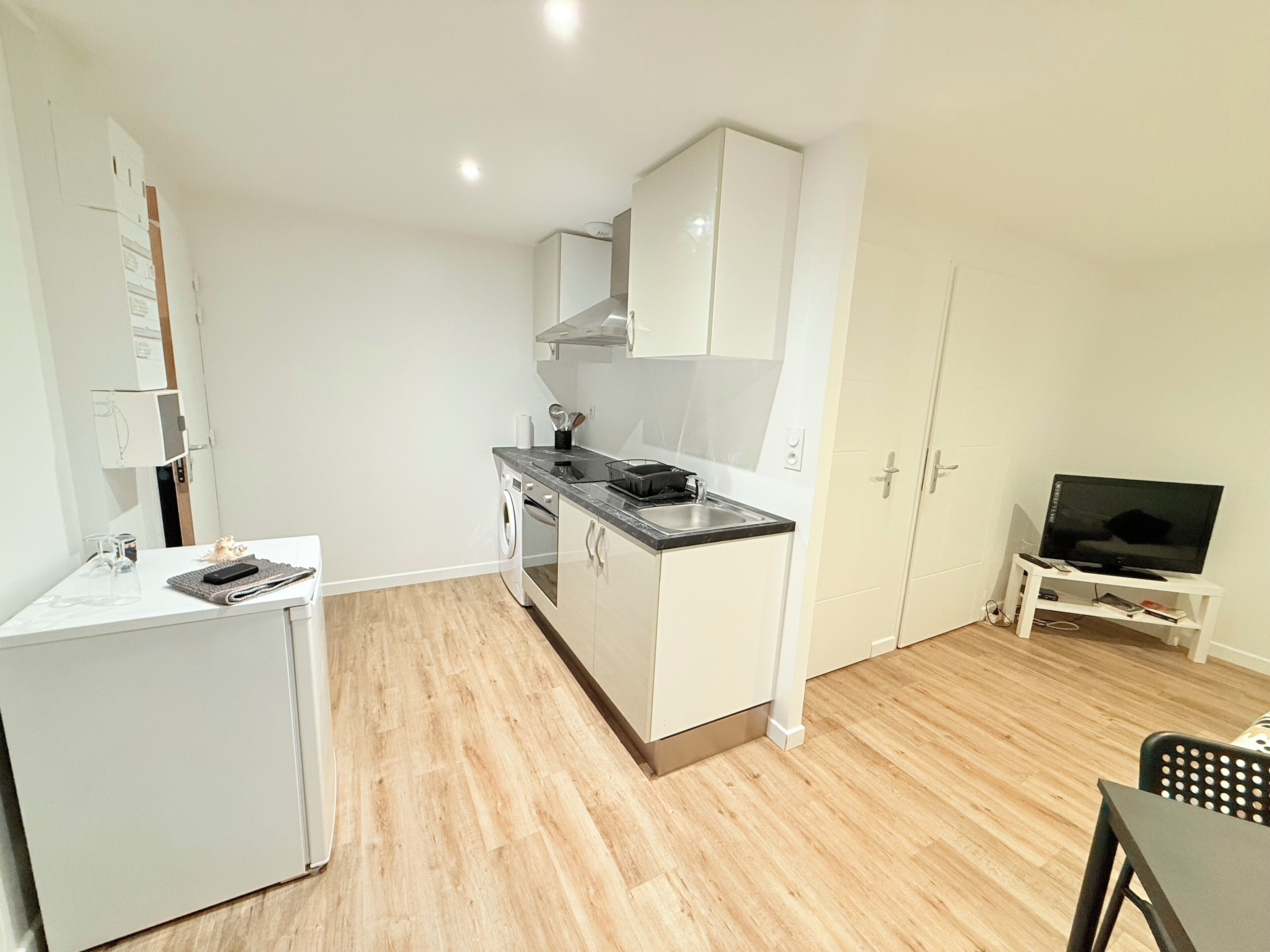 A compact kitchen with a washing machine, a small refrigerator, and a dining area with a TV.
