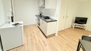 Eine kompakte Küche mit Waschmaschine, kleinem Kühlschrank und Essecke mit Fernseher.