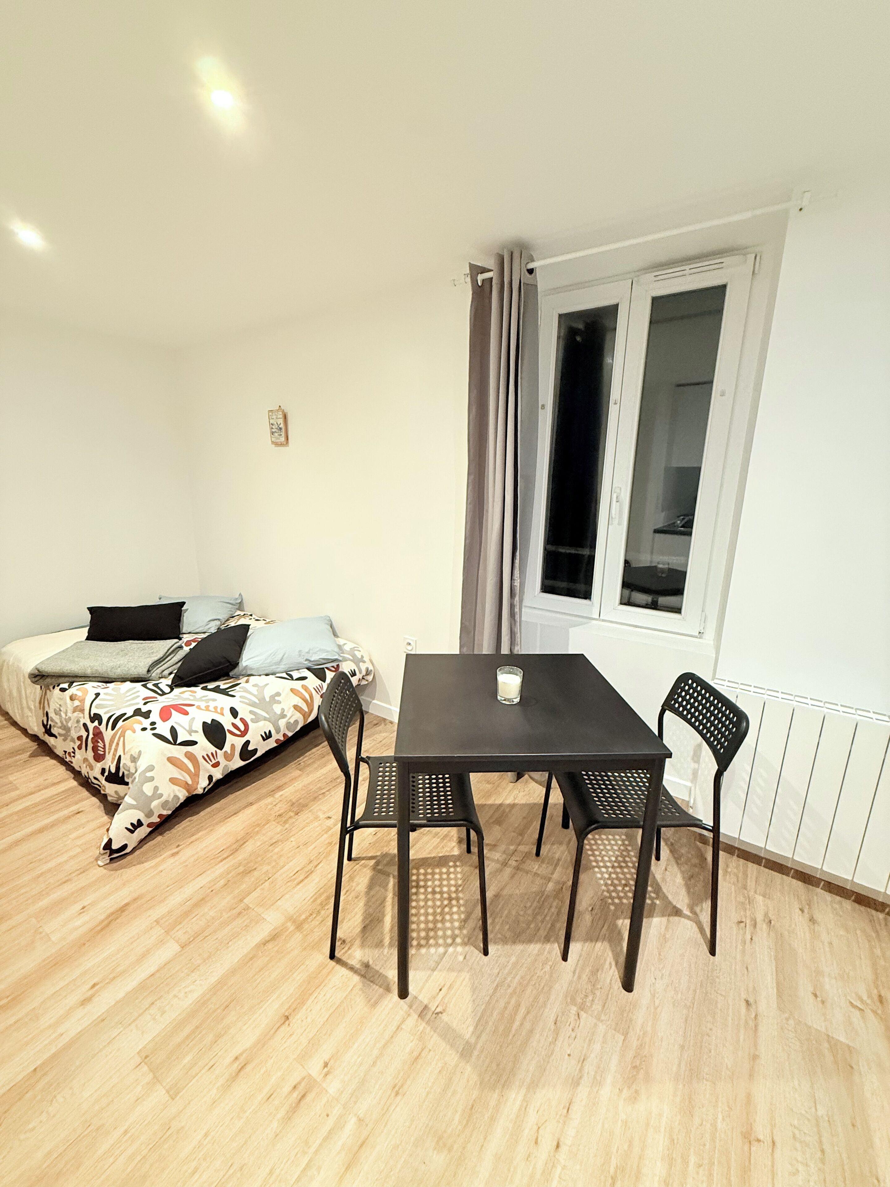 A room with a bed, a table with two chairs, a window with curtains, and a radiator.