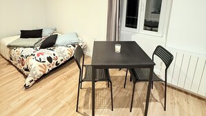 Ein Zimmer mit einem Bett, einem Tisch mit zwei Stühlen, einem Fenster mit Vorhängen und einer Heizung.