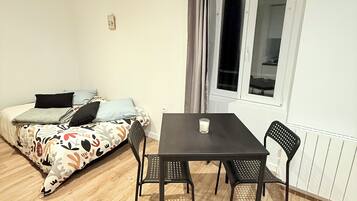 A room with a bed, a table with two chairs, a window with curtains, and a radiator.