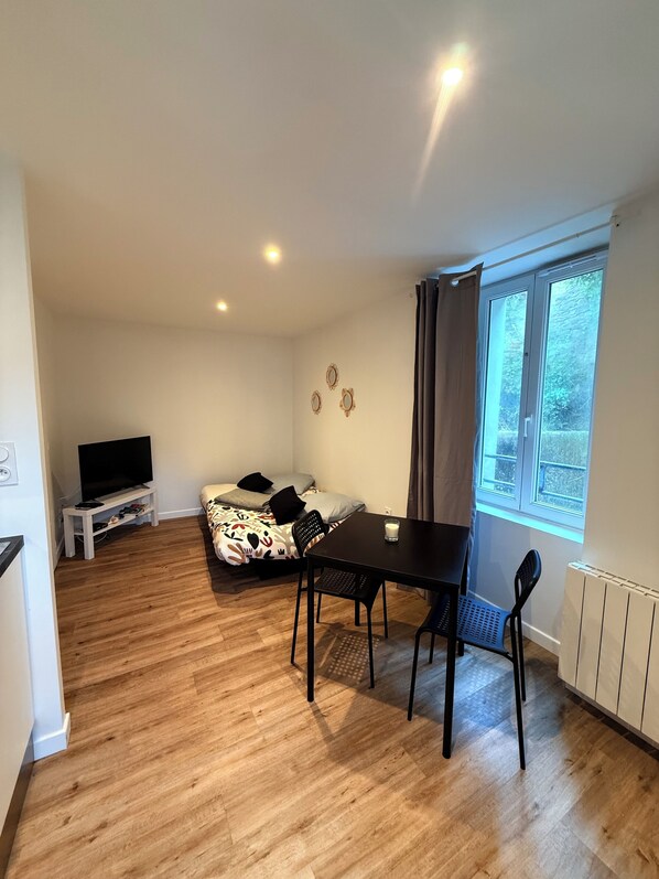 A compact living space with a dining table, chairs, a sofa, a TV, and a window with curtains. - Renovated and fully equipped studio in Belle-Île—in the center of Le Palais (Le Palais)