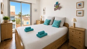 Een slaapkamer met een groot bed, twee nachtkastjes, een houten dressoir, een balkon met uitzicht en een muur met een motiverende quote.