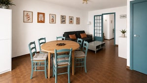 Een moderne woonkamer met een ronde houten tafel, vier stoelen, een bank en een blauwe deur.