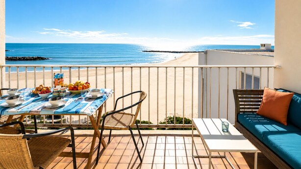 Een balkon met een ontbijttafel, een bank en uitzicht op het strand.