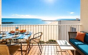 A balcony with a table set for breakfast, a sofa, and a view of the beach. - Mare Nostrum • Family Escape Facing the Sea (MAUGUIO CARNON)