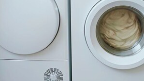 Vista frontal de una lavadora blanca con puerta de vidrio, un panel de control con una perilla y una rejilla circular debajo de la puerta.