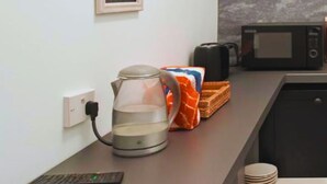 Una encimera de cocina con cafetera, hervidor, microondas y una pila de platos.