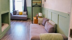 Una habitación con sofá cama, una mesita con lámpara y un perchero.