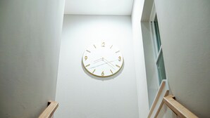 Orologio a parete dal design semplice, situato in un corridoio con pareti bianche e corrimano in legno.