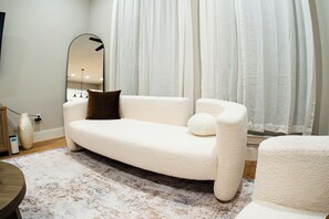 A modern living room with a white sofa, a round coffee table, a large mirror, and sheer curtains. - Luxury 3 Story Townhome 2 Bed, 4 Bath Fully Furnished 3 min from downtown Dallas (Dallas)