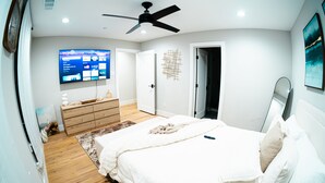 Una camera da letto con un letto, una TV montata a muro, una ventola a soffitto e una porta che dà su un'altra stanza.