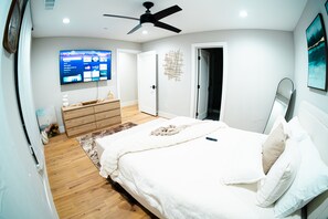 Ein Schlafzimmer mit einem Bett, einem an der Wand befestigten Fernseher, einem Deckenventilator und einer Tür zu einem anderen Raum.