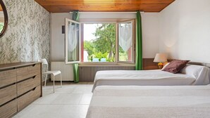 Une chambre avec deux lits, une commode, une chaise, une fenêtre avec des rideaux et une lampe.