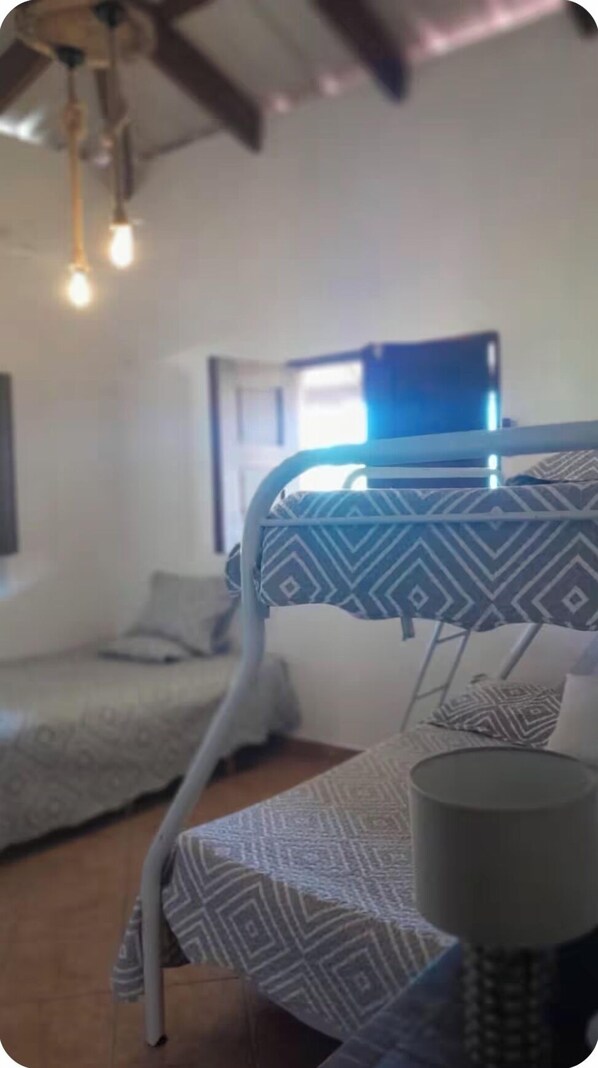 Una habitación con literas, una ventana con cortinas, una lámpara colgante y un mantel estampado.