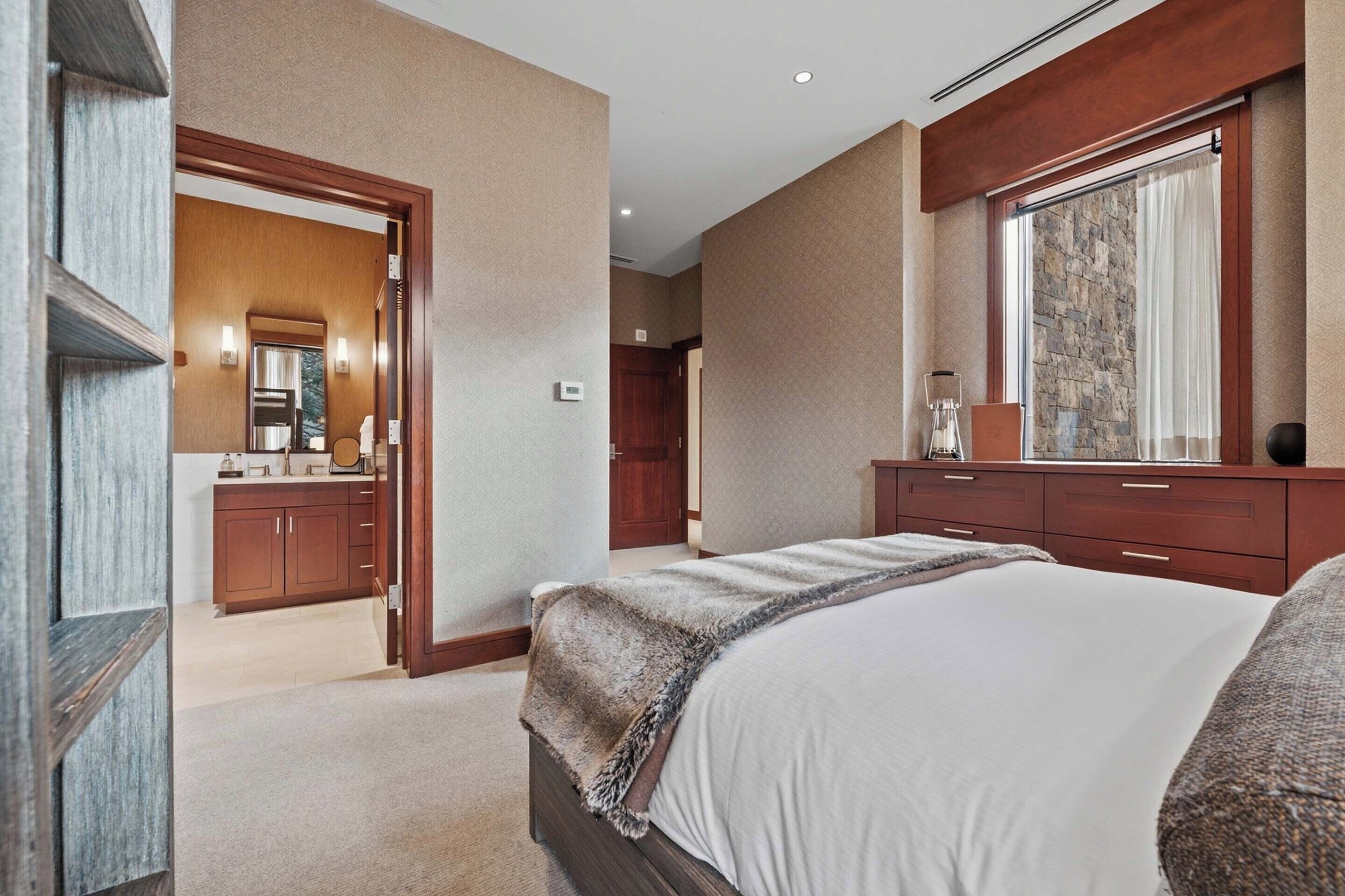 Een moderne hotelkamer met een groot bed, een houten dressoir, een spiegel en uitzicht op de badkamer.