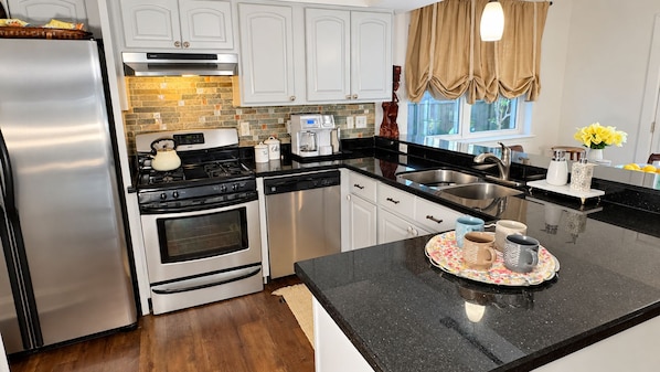 A modern kitchen with stainless steel appliances, a coffee maker, and a window with curtains.