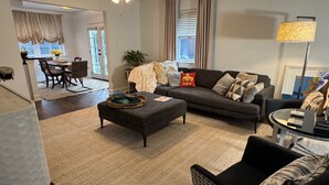 Ein Wohnzimmer mit einer Couch, Hocker und einem Essbereich mit Stühlen und Tisch.
