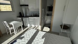 Une pièce de taille modeste comprenant un lit, un coin cuisine et un petit espace repas.