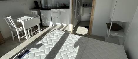 A compact room with a bed, kitchenette, and a small dining area.