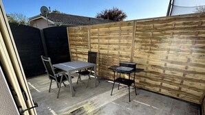 Un espace patio doté d’un sol en béton, d’une clôture en bois et de deux tables avec des chaises.