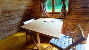 A wooden cabin interior with a dining table and chairs, a window with curtains, and a view of greenery outside. - Chez Tombivouac (Pierrefonds)