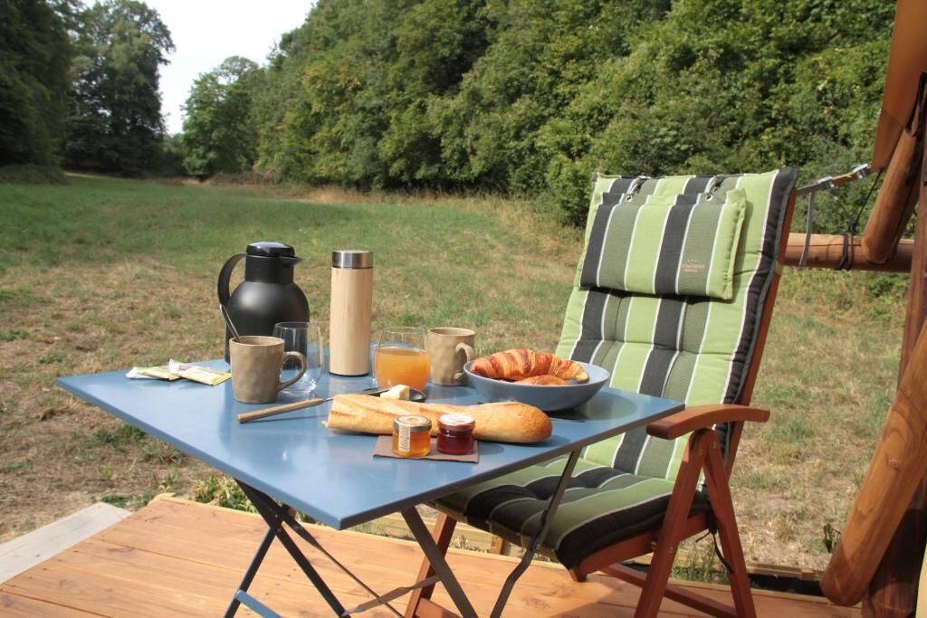 A picnic setup with a table, a chair, and food items including a croissant, bread, and a bottle of juice.