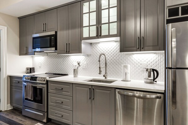 Una cocina moderna con electrodomésticos de acero inoxidable, armarios grises y salpicadero de azulejos blancos.