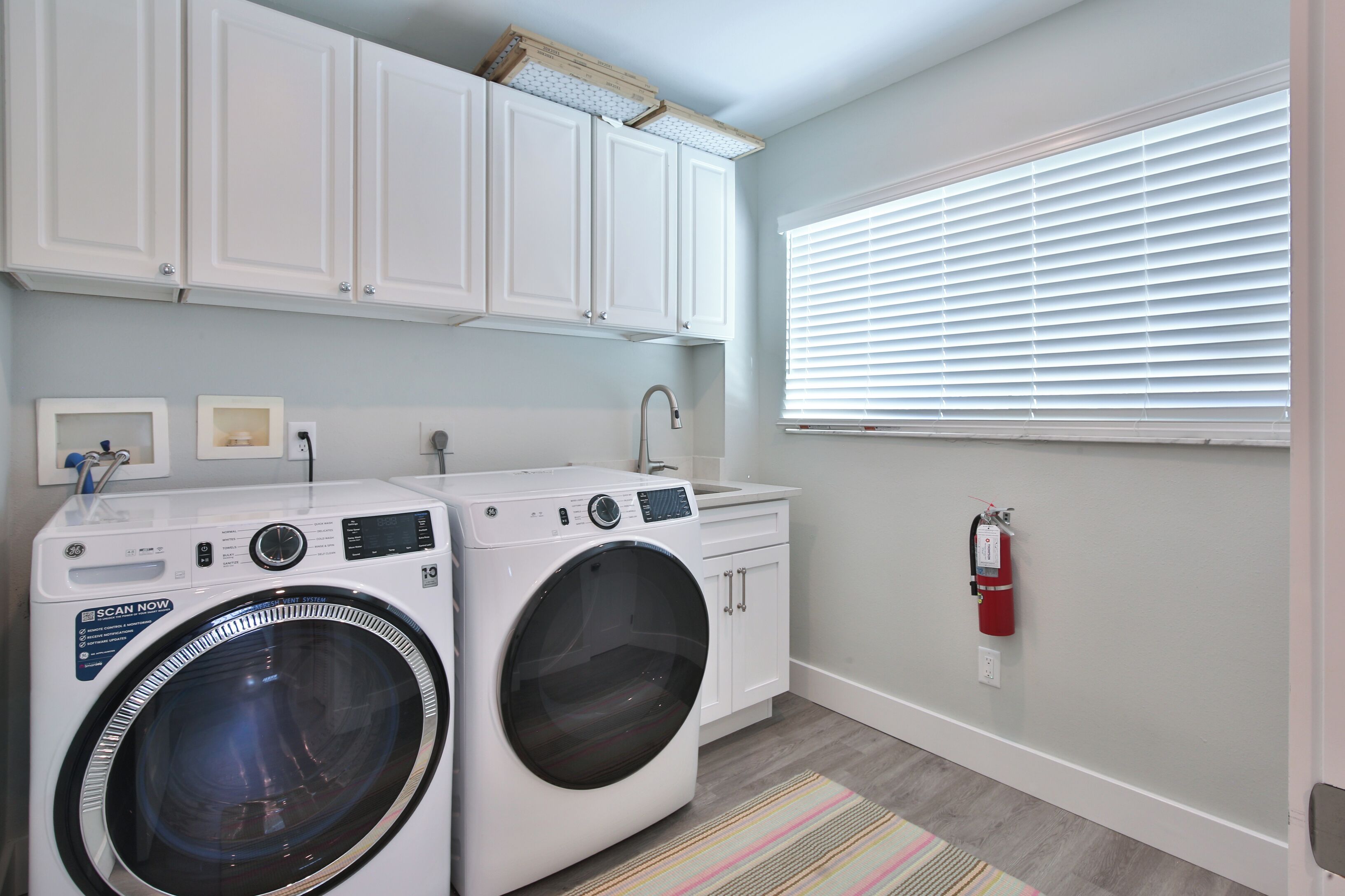 A laundry room with two front-loading washing machines, a sink, and a fire extinguisher.