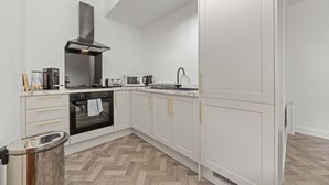 A modern kitchen with white cabinetry, a black range hood, and a herringbone-patterned floor. - The Manor - Beachwalk Apartments (North Lanarkshire)
