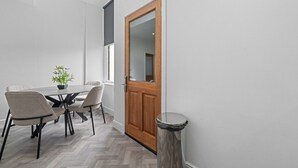 A modern interior with a dining area featuring a table and chairs, a potted plant, and a wooden door with a mirror. - The Manor - Beachwalk Apartments (North Lanarkshire)