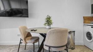 Una cocina moderna con una mesa redonda de comedor, dos sillas, una planta en maceta, una lavadora y un televisor montado en la pared.