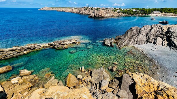 Un paysage côtier caractérisé par des eaux limpides, des formations rocheuses et une ligne de côte lointaine où se dressent des bâtiments.