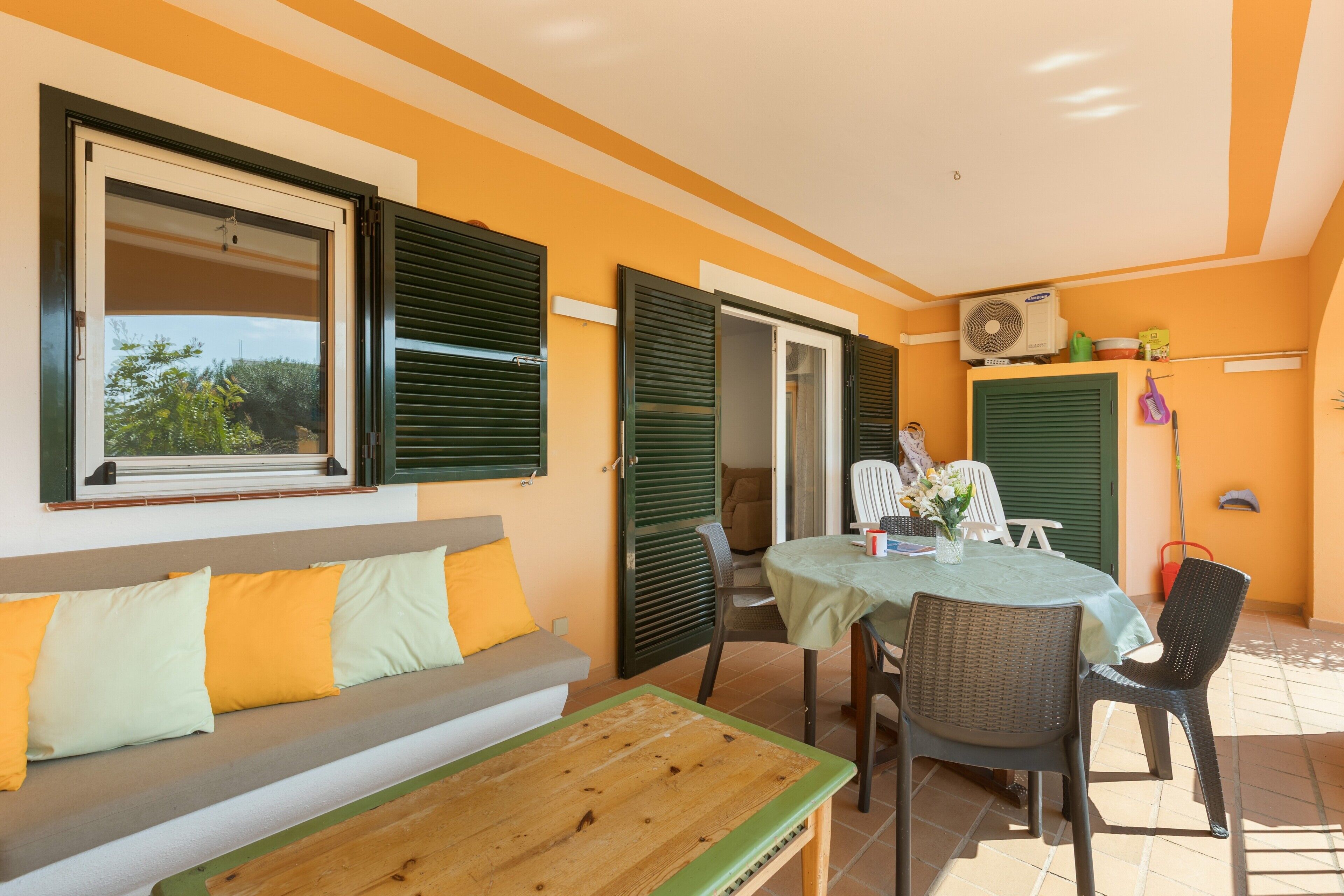 Quarto com sofá, mesa, cadeiras, janela com persianas e ar condicionado.