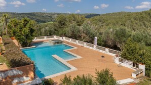 Une piscine rectangulaire dotée d’une terrasse blanche et d’une clôture blanche, entourée de verdure et de collines.