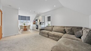 Una sala de estar moderna con un sofá gris, un comedor con mesa y sillas, y una cocina al fondo.