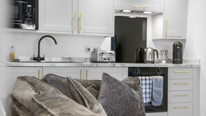 A modern kitchen with white cabinets, a black microwave, a coffee maker, and a toaster. - The Snug | Beachwalk Apartments by Nova Suites (South Ayrshire)
